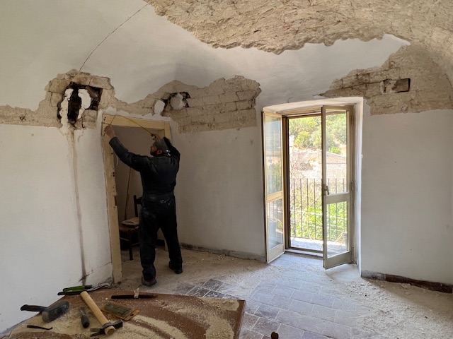 Worker restoring a historic Italian ceiling by removing plaster, revealing the original brickwork and architectural features