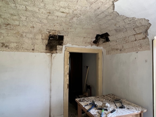 Worker restoring a historic Italian ceiling by removing plaster, revealing the original brickwork and architectural features