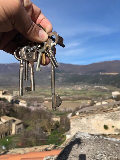 Hand holding old keys with a panoramic view of the Italian countryside in the background, symbolizing home ownership and new beginnings