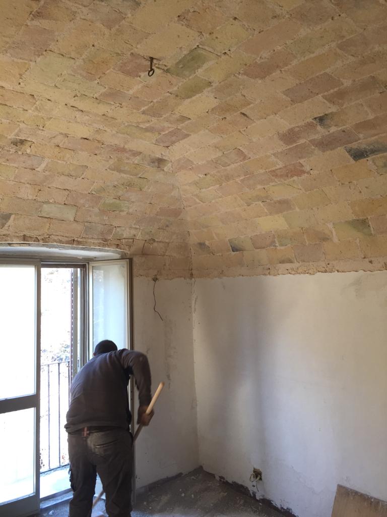 Worker restoring an exposed brick dome ceiling in an Italian home, carefully removing plaster