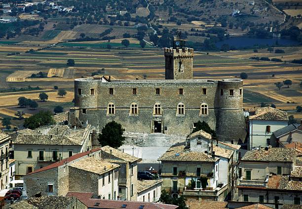 Aerial view of Castello Piccolomini, a historic medieval castle surrounded by a quaint Italian village and rolling farmland