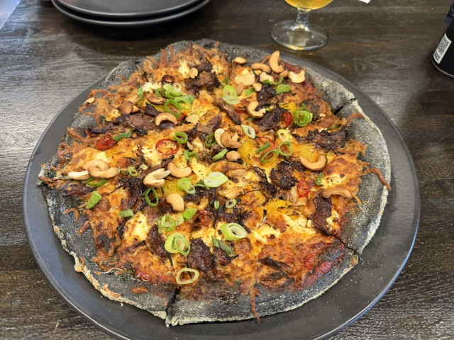 Black-crust pizza topped with meat, cashews, peppers and green onions during our Iceland campervan trip.
