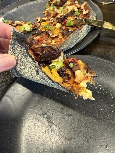 Slice of black-crust pizza showing the dark crust and toppings during our Iceland road trip.